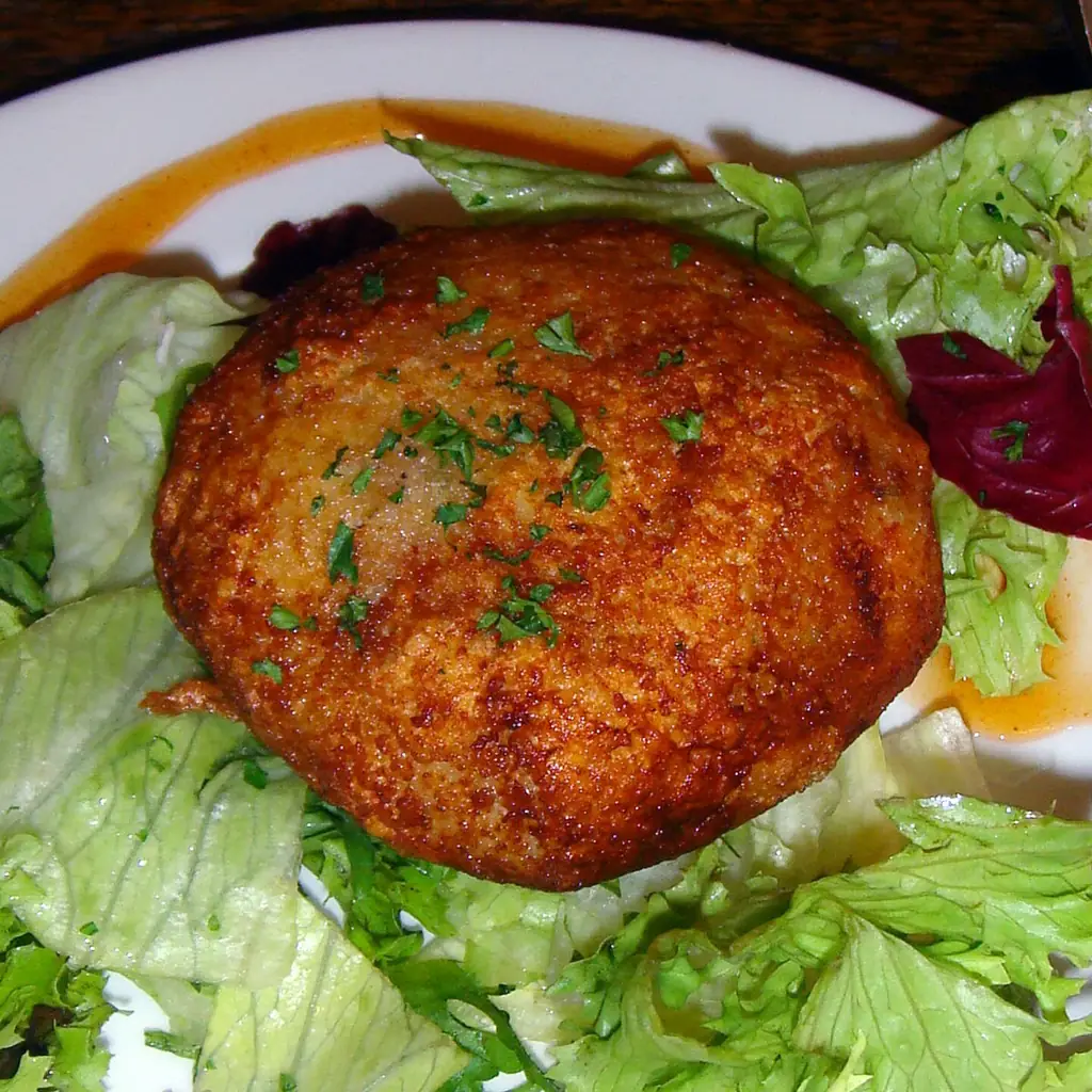 A browned fish cake served on green salad leaves.
