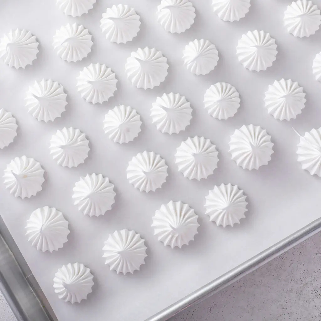 Small white meringue kisses arranged on a baking tray.