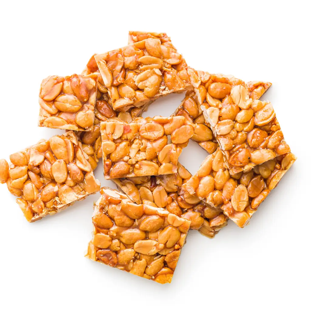 Pieces of golden peanut brittle with visible peanuts.