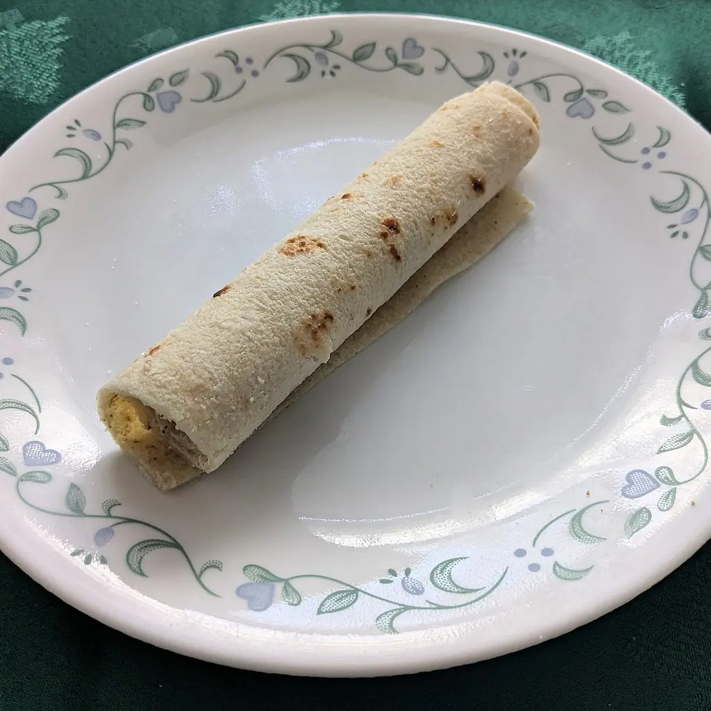A rolled piece of lefse on a patterned plate.