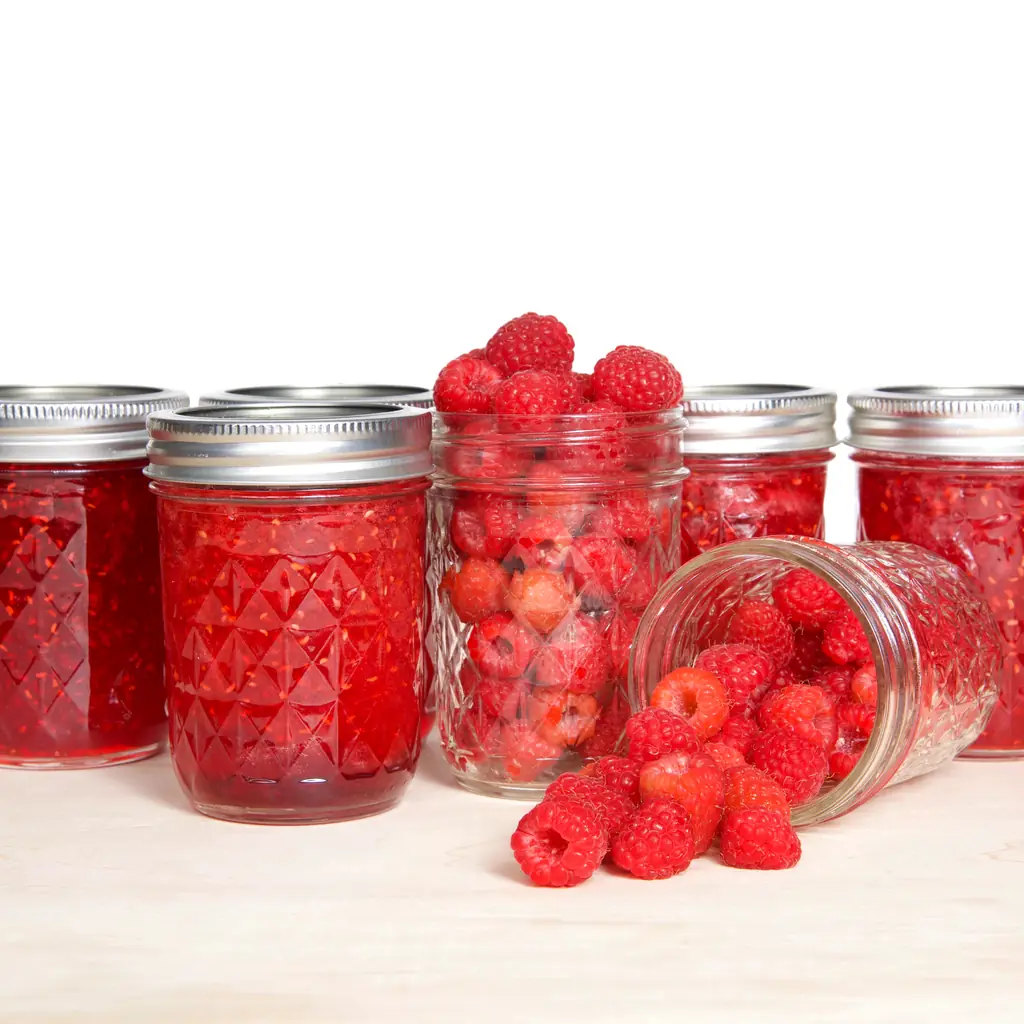 Glass jars of raspberry preserves beside fresh raspberries.