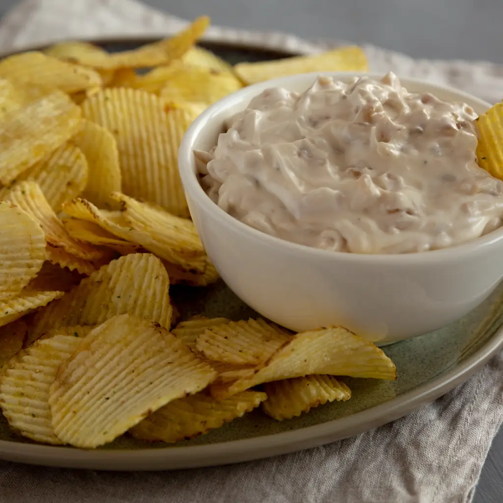 French onion dip in a white bowl beside ridged potato chips.