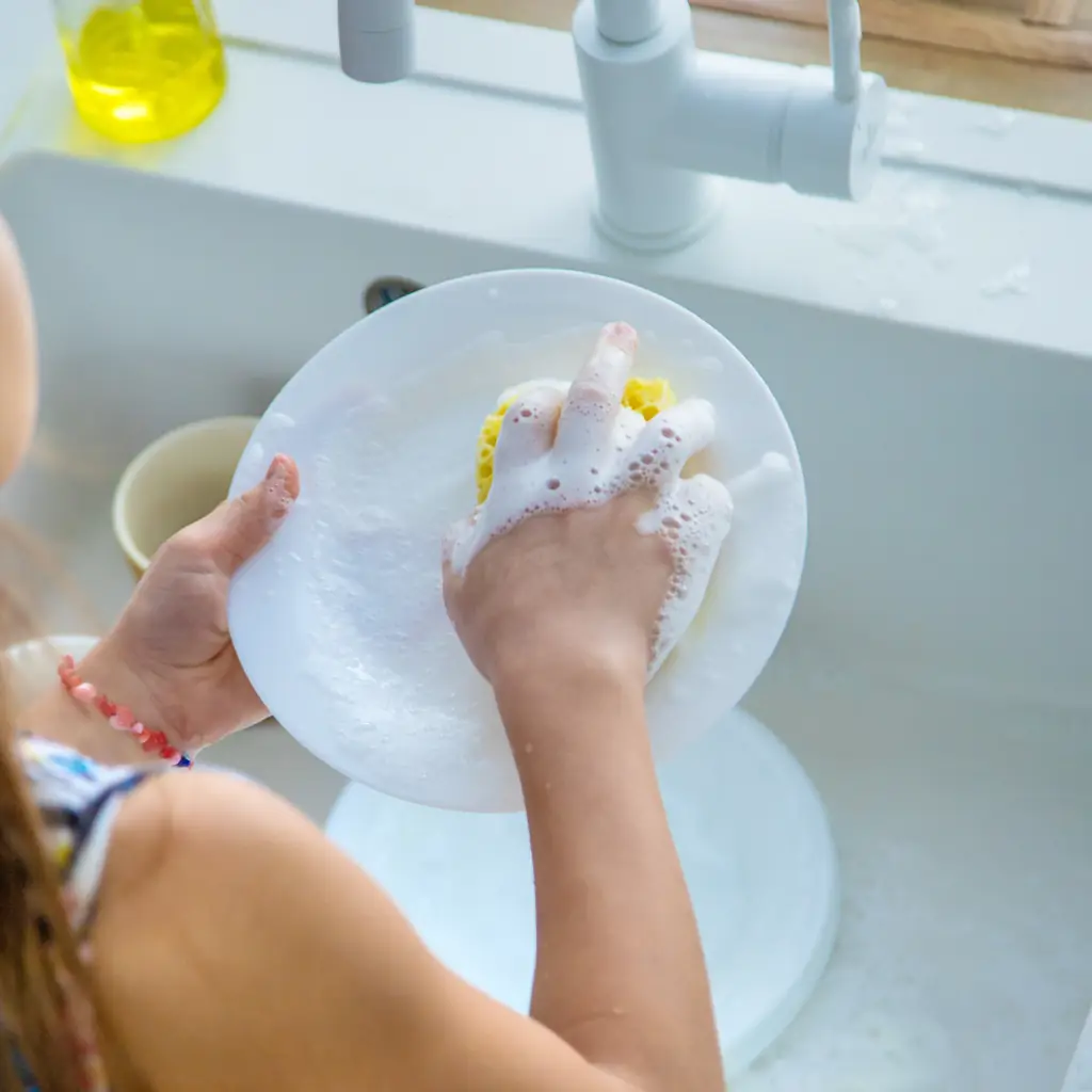 A child washing a white plate in a kitchen sink.