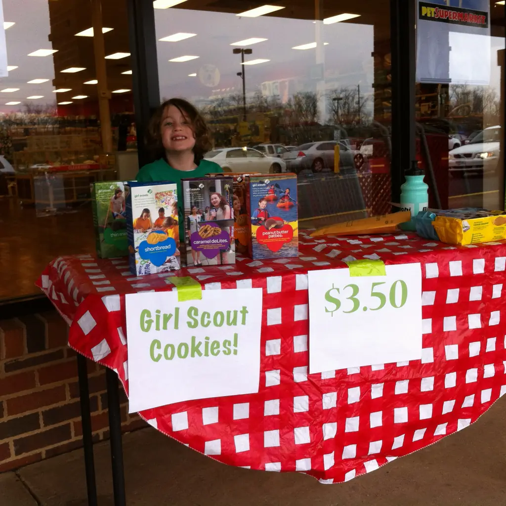 A Girl Scout cookie table with boxes of cookies at a shop entrance.